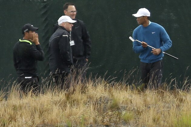 Golfer Tiger Woods, right, walks past a fence as rain begins to fall, Tuesday, June 2, 2015, as he took practice shots at Chambers Bay in University Place, Wash., where the U.S. Open will be played June 18-21, 2015. (AP Photo/Ted S. Warren)