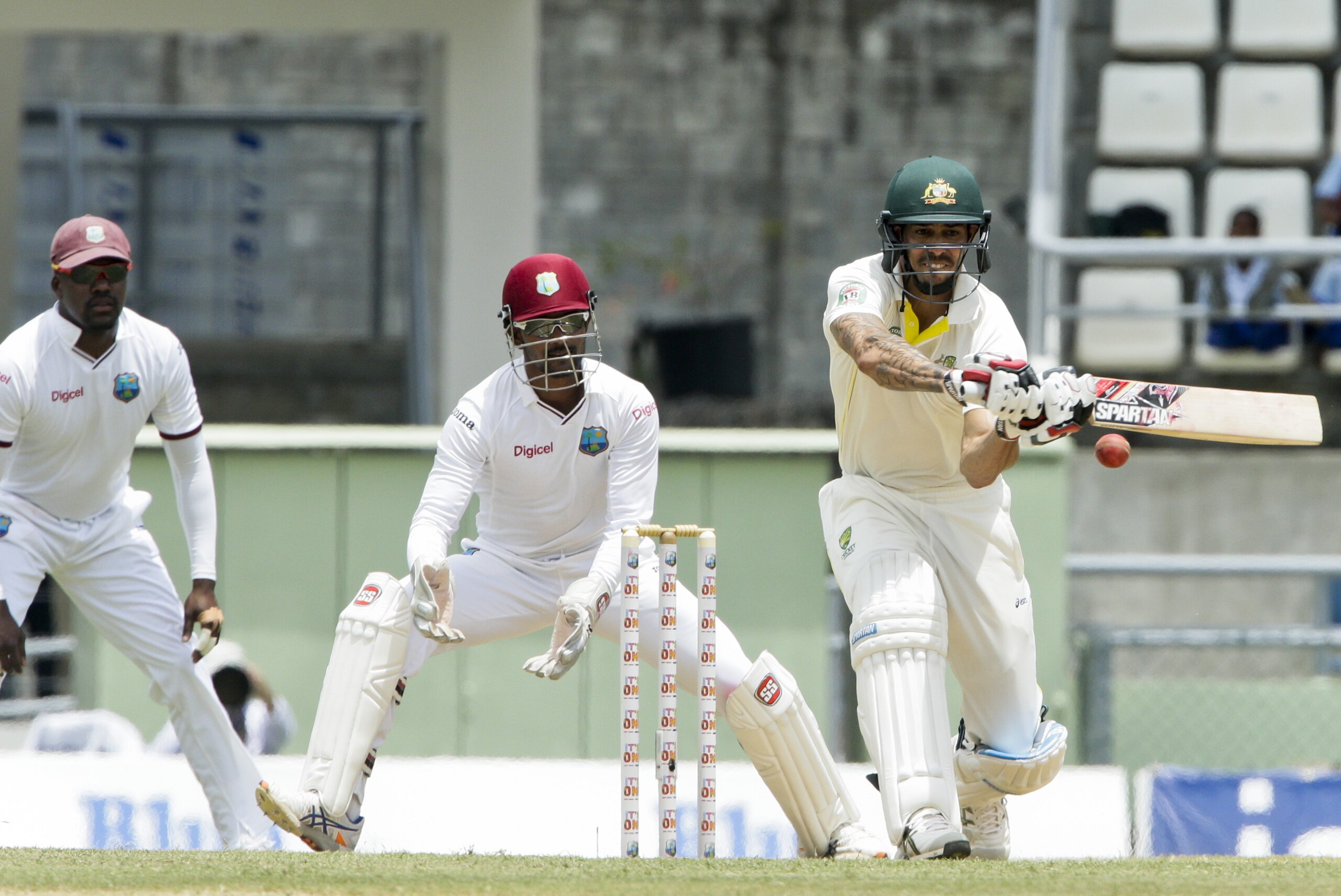 Australia's Mitchell Johnson, right, bats as West Indies wicket keeper, captain Denesh Ramdin, center, and Darren Bravo, left, looks on, during the second day of their first cricket Test match in Roseau, Dominica, Thursday, June 4, 2015. (AP Photo/Arnulfo Franco)