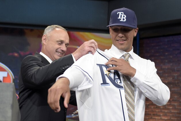 Commissioner of Major League Baseball Rob Manfred, left, helps outfielder Garrett Whitley from Niskayuna High School in Niskayuna, N.Y., put on his Tampa Bay Rays jersey at the 2015 MLB baseball draft Monday, June 8, 2015, in Secaucus, N.J. Whitley was chosen by the Rays with the 13th selection. (AP Photo/Bill Kostroun)
