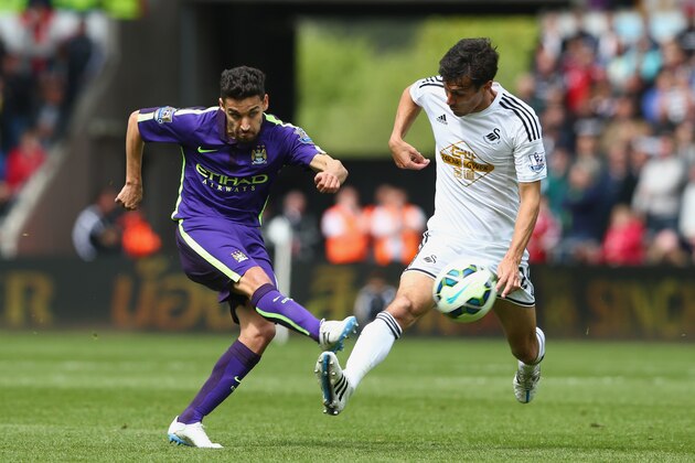 SWANSEA, WALES - MAY 17:  Jesus Navas of Manchester City takes a shot as Ashley Richards of Swansea City closes in during the Barclays Premier League match between Swansea and Manchester City at the Liberty Stadium on May 17, 2015 in Swansea, Wales.  (Photo by Michael Steele/Getty Images)