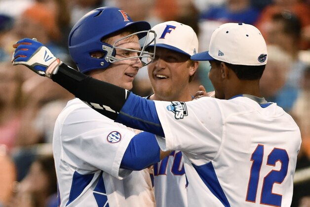 Florida's Peter Alonso, left, is greeted by Richie Martin (12), after scoring on a single by Mike Rivera during the fourth inning of an NCAA College World Series baseball game against Miami at TD Ameritrade Park in Omaha, Neb., Saturday, June 13, 2015. (AP Photo/Mike Theiler)