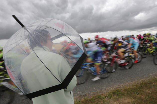 A woman watches the pack pass as she takes cover under an umbrella during the fifth stage of the Tour de France cycling race over 189.5 kilometers (117.8 miles) with start in Arras and finish in Amiens, France, Wednesday, July 8, 2015. (AP Photo/Christophe Ena)