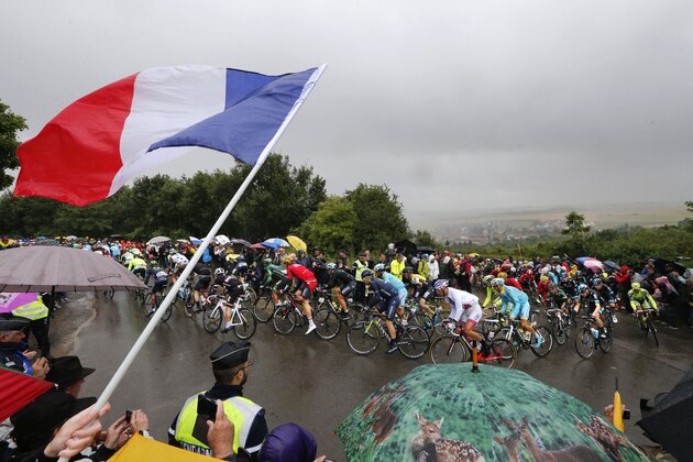 A spectator waves the French flag as the pack climbs in the rain during the fifth stage of the Tour de France cycling race over 189.5 kilometers (117.8 miles) with start in Arras and finish in Amiens, France, Wednesday, July 8, 2015. (AP Photo/Christophe Ena)