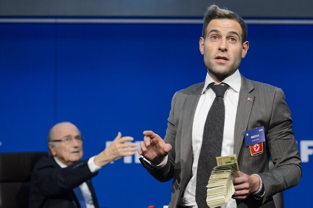 British comedian Lee Nelson (R) holds fake dollars note next to FIFA president Sepp Blatter gestures during a protest at a press conference at the football's world body headquarter's on July 20, 2015 in Zurich. A British comedian on interrupted a press conference by Sepp Blatter in Zurich throwing paper money in front of the bemused FIFA president just as he was about to speak.  AFP PHOTO / FABRICE COFFRINI        (Photo credit should read FABRICE COFFRINI/AFP/Getty Images)