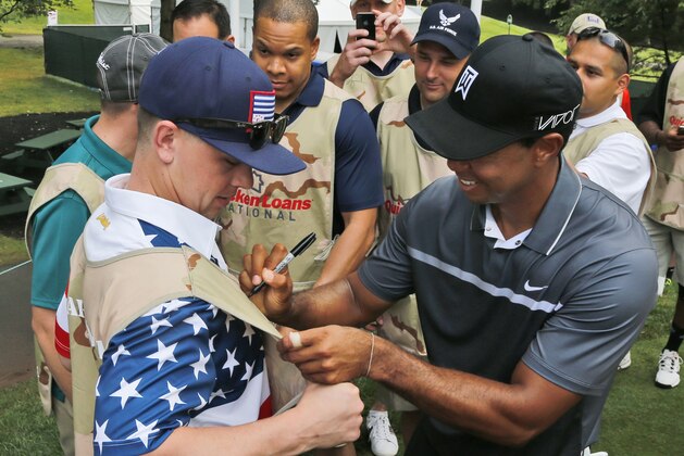 Tiger Woods autographs the vest of military caddie Coast Guard petty officer Chris Hopp, of Chicago, during the pro-am for the Quicken Loans National Golf tournament at the Robert Trent Jones Golf Club in Gainesville, Va., Wednesday, July 29, 2015.  (AP Photo/Steve Helber)
