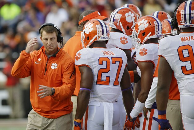 Clemson head coach Dabo Swinney adjusts his headphones while huddling with his team during a timeout in the first quarter of their NCAA college football game against Boston College at Alumni Stadium on the Boston College Campus Saturday, Oct. 18, 2014 in Boston. (AP Photo/Stephan Savoia)