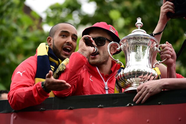 Arsenal's English midfielder Jack Wilshere (R) and Arsenal's English midfielder Theo Walcott hold the trophy as they stand on the top deck of an open-topped bus during the Arsenal victory parade in London on May 31, 2015, following their win in the English FA Cup final football match on May 30, 2014 against Aston Villa. Arsene Wenger's side made history at Wembley with a 4-0 rout of Aston Villa that underlined their renaissance in the second half of the campaign and served as a warning to English champions Chelsea.     AFP PHOTO / LEON NEAL        (Photo credit should read LEON NEAL/AFP/Getty Images)