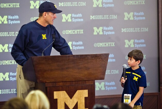 Michigan head coach Jim Harbaugh, left, listens to a question from first grader Brady Carpenter, right, at a press conference during the NCAA college football team's annual media day in Ann Arbor, Mich., Thursday, Aug. 6, 2015. Five children were picked in a contest to ask questions of the Michigan coach. (AP Photo/Tony Ding)