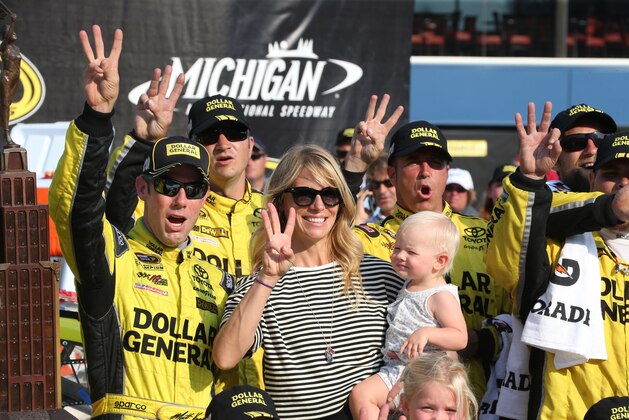 Matt Kenseth stands with his wife, Katie, and team members after winning the NASCAR Sprint Cup series auto race at Michigan International Speedway, Sunday, Aug. 16, 2015, in Brooklyn, Mich. (AP Photo/Bob Brodbeck)