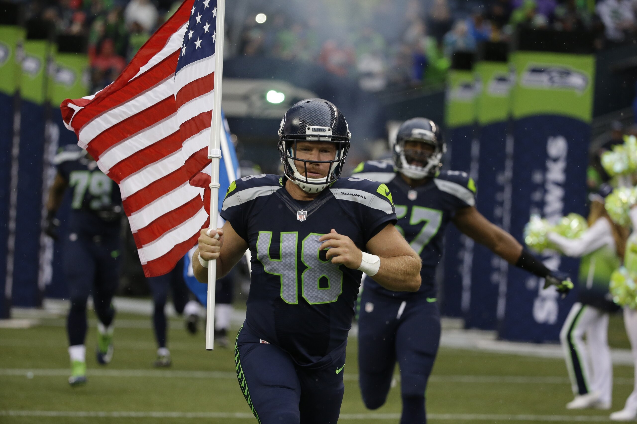 Seattle Seahawks long snapper and military veteran Nate Boyer runs out of the tunnel with a U.S. flag at the start of a preseason NFL football game against the Denver Broncos, Friday, Aug. 14, 2015, in Seattle. (AP Photo/Elaine Thompson)