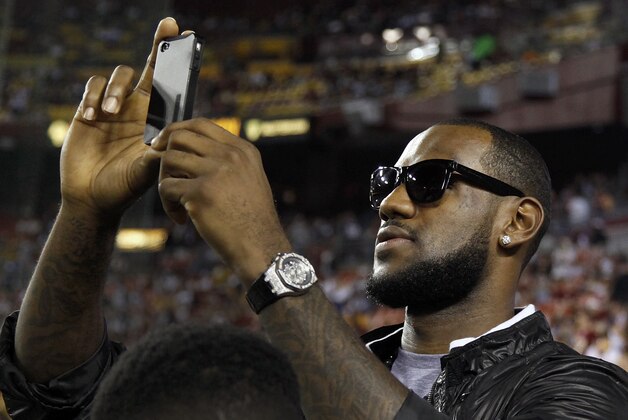 Basketball player LeBron James shoots a video with his cell phone from the sidelines before an NFL football game between the Dallas Cowboys and Washington Redskins in Landover, Md., on Sunday, Sept. 12, 2010.  (AP Photo/Evan Vucci)