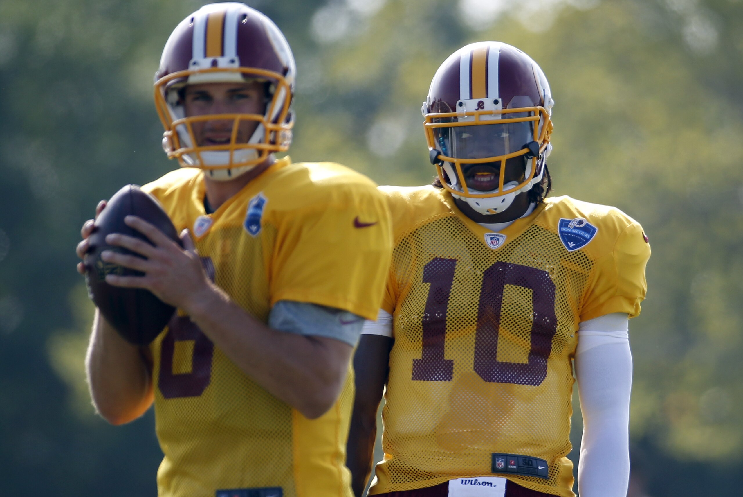 Washington Redskins quarterback Kirk Cousins prepares to pass as quarterback Robert Griffin III watches, during practice at the team's NFL football training facility, Saturday, July 26, 2014 in Richmond, Va. (AP Photo/Alex Brandon)