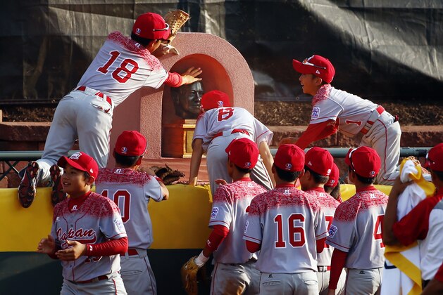 Japan players leap onto the centerfield fence to touch a bust of Howard Lamade after the Little League World Series Championship baseball game against Lewisberry, Pa. in South Williamsport, Pa., Sunday, Aug. 30, 2015. Japan won 18-11. (AP Photo/Gene J. Puskar)
