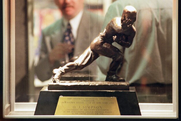 ** FILE ** Michael Schwartz, director of entertainment memorabilia for the auction house of Butterfield & Butterfield, is seen through a display case containing O.J. Simpson's 1968 Heisman Trophy at their gallery in this Feb. 10, 1999 file photo, in Los Angeles. The auction house conducted a court-ordered auction of Simpson items in 1999 to help pay off a $33.5-million award won by the Brown and Goldman families in a wrongful death lawsuit. Simpson's 1968 Heisman Trophy was sold for $255,500 to Tom Kriessman, a Philadelphia steel company owner who said he purchased it as an investment and to impress his girlfriend.  (AP Photo/Rene Macura, File)