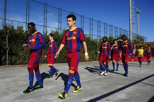 Barcelona soccer club youth players Brian Olivan, foreground, and Jean Marie Dongou of Cameroon, left, lead their team onto the field to play against Reus Deportiu at the Barcelona FC's Joan Gamper training camp in San Joan Despi, Spain, on Saturday, Jan. 8, 2011. Xavi Hernandez, Andres Iniesta or Lionel Messi will win FIFA's Ballon d'Or trophy as the world's best player on Monday, and much of the teammates' success can be attributed to Barcelona's La Masia youth academy. (AP Photo/Manu Fernandez)