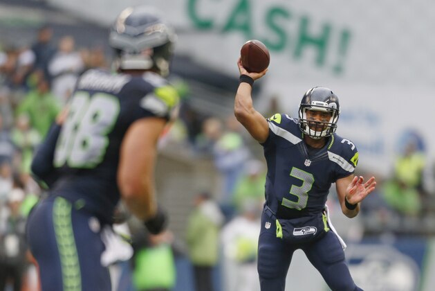 With a stadium advertisement in the background, Seattle Seahawks quarterback Russell Wilson (3) completes a pass to Seattle Seahawks tight end Jimmy Graham in the first half of a preseason NFL football game against the Denver Broncos, Friday, Aug. 14, 2015, in Seattle. (AP Photo/John Froschauer)