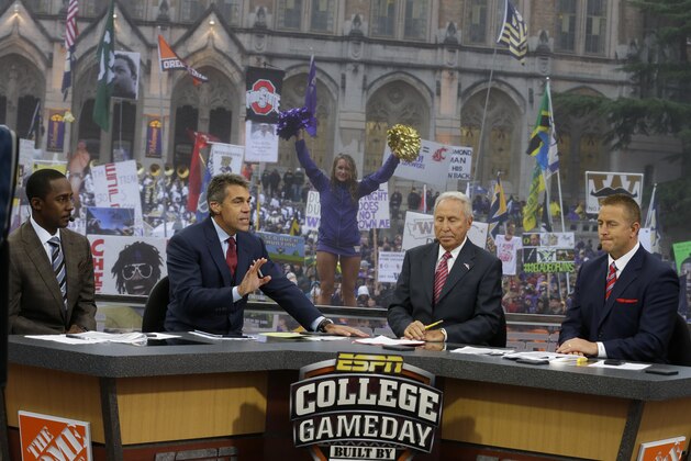 ESPN College GameDay host Lee Corso, second from right, talks with co-hosts Desmond Howard, left, Chris Fowler, second from left, and Kirk Herbstreit, right, Saturday, Oct. 12, 2013, during College GameDay's broadcast from Red Square on the University of Washington campus in Seattle before an NCAA college football game between Washington and Oregon. (AP Photo/Ted S. Warren)