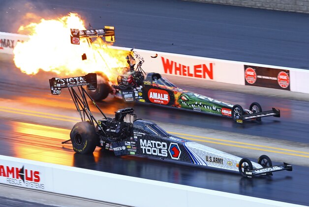 Sep 20, 2015; Concord, NC, USA; NHRA top fuel driver Antron Brown (near) races alongside Terry McMillen explodes an engine on fire during the Carolina Nationals at zMax Dragway. Mandatory Credit: Mark J. Rebilas-USA TODAY Sports