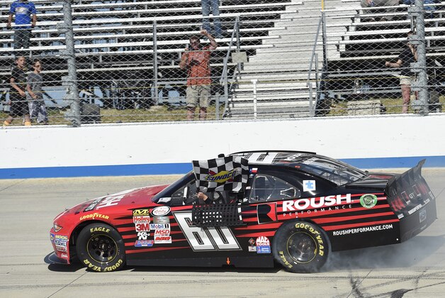 Chris Buescher waves the checkered flag as he drives by the stands and celebrates after he won the NASCAR Xfinity series auto race, Saturday, May 30, 2015, at Dover International Speedway in Dover, Del. (AP Photo/Nick Wass)
