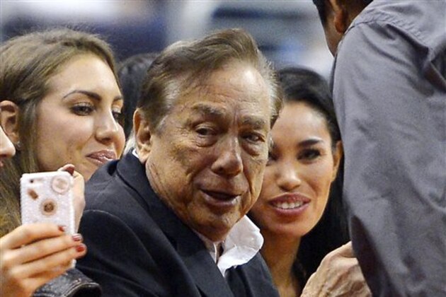 In this photo taken on Friday, Oct. 25, 2013, Los Angeles Clippers owner Donald Sterling, center, and V. Stiviano, right, watch the Clippers play the Sacramento Kings during the first half of an NBA basketball game, in Los Angeles. The NBA is investigating a report of an audio recording in which a man purported to be Sterling makes racist remarks while speaking to Stiviano.  NBA spokesman Mike Bass said in a statement Saturday, April 26, 2014, that the league is in the process of authenticating the validity of the recording posted on TMZ's website. Bass called the comments