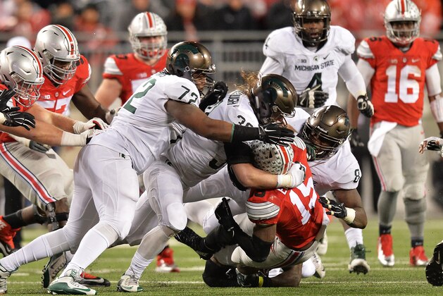 COLUMBUS, OH - NOVEMBER 21:  Ezekiel Elliott #15 of the Ohio State Buckeyes is gang tackled by Craig Evans #72 of the Michigan State Spartans, Riley Bullough #30 of the Michigan State Spartans and Lawrence Thomas #8 of the Michigan State Spartans in the third quarter at Ohio Stadium on November 21, 2015 in Columbus, Ohio. Michigan State defeated Ohio State 17-14.  (Photo by Jamie Sabau/Getty Images)