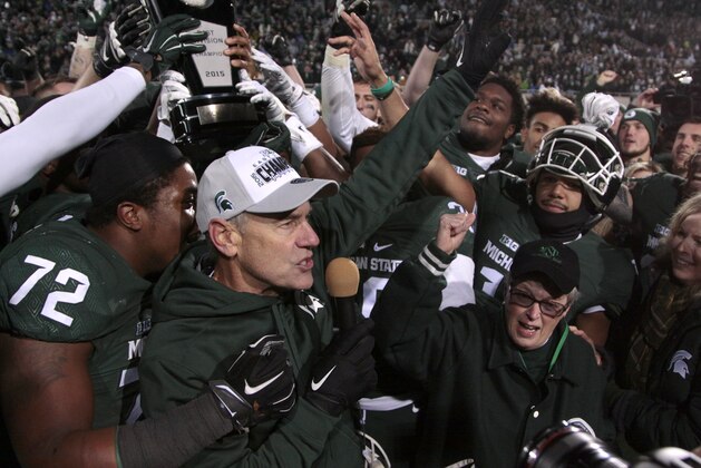 Michigan State coach Mark Dantonio, left, university president Lou Anna Simon, bottom right, and players celebrate with their Big Ten East Division Championship trophy after beating Penn State 55-16 in an NCAA college football game, Saturday, Nov. 28, 2015, in East Lansing, Mich.  (AP Photo/Al Goldis)