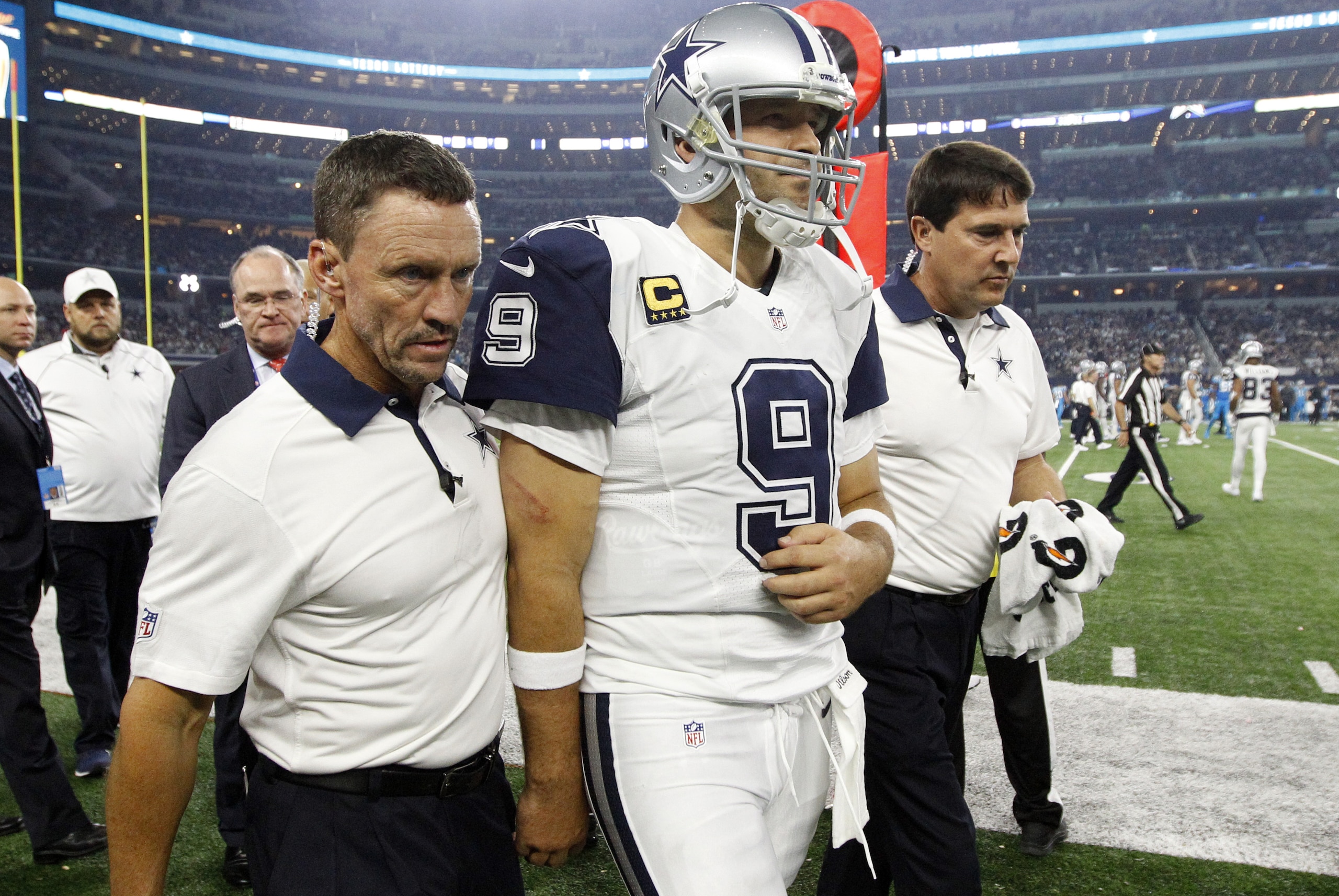 Team staff escort Dallas Cowboys quarterback Tony Romo (9) off the field after Romo suffered an unknown injury after being sacked by Carolina Panthers outside linebacker Thomas Davis in the second half of an NFL football game, Thursday, Nov. 26, 2015, in Arlington, Texas. (AP Photo/Brandon Wade)