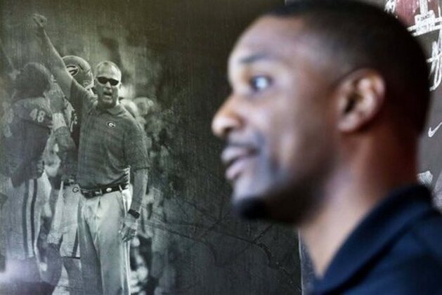 A mural of former Georgia football head coach Mark Richt stands in the background as interim head coach Bryan McClendon, right, speaks during a press conference Wednesday, Dec. 16, 2015, in Athens, Ga. A coaching change at Georgia has left McClendon with a smaller staff as practice begins Wednesday for the TaxSlayer Bowl game against Penn State. Richt, the longtime head coach, was let go after the regular season and is now at Miami. (AP Photo/David Goldman)