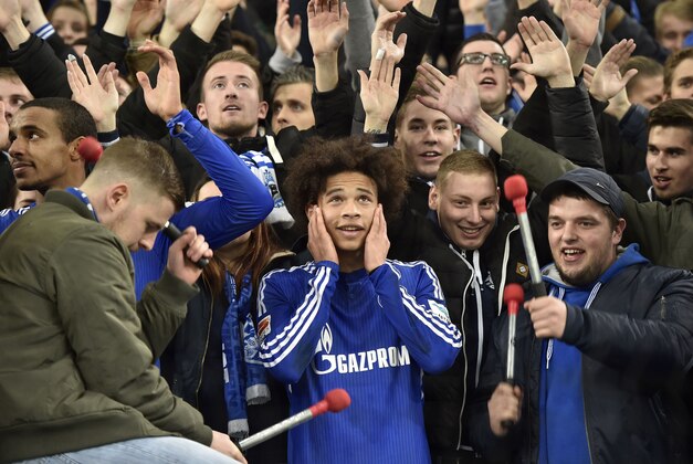 Schalke's Leroy Sane, center, holds his ears between supporters in the fan curve after the German Bundesliga soccer match between FC Schalke 04 and Hannover 96 in Gelsenkirchen, Germany, Friday, Dec. 4, 2015. Schalke defeated Hannover with 3-1.(AP Photo/Martin Meissner)