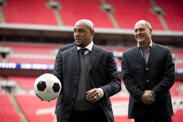 Former Brazil national soccer team player Roberto Carlos holds a ball as he attends a group photo session pitchside as a guest of FIFA Presidential Candidate Gianni Infantino after unveiling his 90 day plan that he will implement if he is elected FIFA President, at Wembley Stadium in London, Monday, Feb. 1, 2016. (AP Photo/Matt Dunham)
