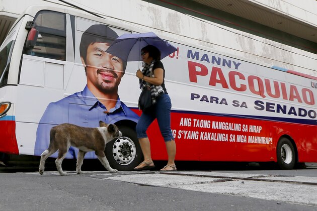 A dog and woman walks past a bus with an image of senatorial candidate and boxer Manny Pacquiao that will be used for campaigning for the May 9 national elections Saturday, Feb. 20, 2016 in Manila, Philippines. Pacquiao was criticized for his remarks regarding people in same-sex relationships. (AP Photo/Bullit Marquez)