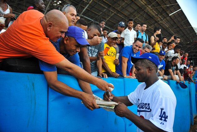 Cuban MLB player Yasiel Puig (R) signs autographs at the Latin American Stadium in Havana, on December 16, 2015. Cuban baseball stars Jose Abreu and Yasiel Puig returned home Tuesday for the first time since defecting to join the American big leagues, part of an unprecedented Major League Baseball tour made possible by the thaw in US-Cuban relations. The delegation also includes Cuban-born player Alexei Ramirez, a free agent who left Cuba legally by marrying a Dominican in 2007.    AFP PHOTO/YAMIL LAGE / AFP / YAMIL LAGE        (Photo credit should read YAMIL LAGE/AFP/Getty Images)