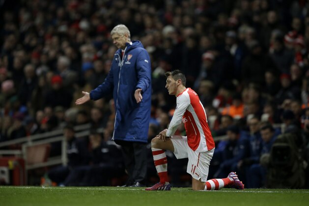 Arsenal's Mesut Ozil, right, gets up after a challenge, backdropped by his French manager, Arsene Wenger during the English Premier League soccer match between Arsenal and Leicester City at the Emirates Stadium in London, Tuesday, Feb. 10, 2015.  (AP Photo/Matt Dunham)