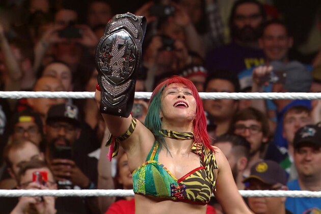 Asuka hoists her new belt above her head.