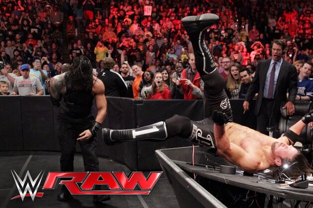 Roman Reigns powerbombs AJ Styles through a table.