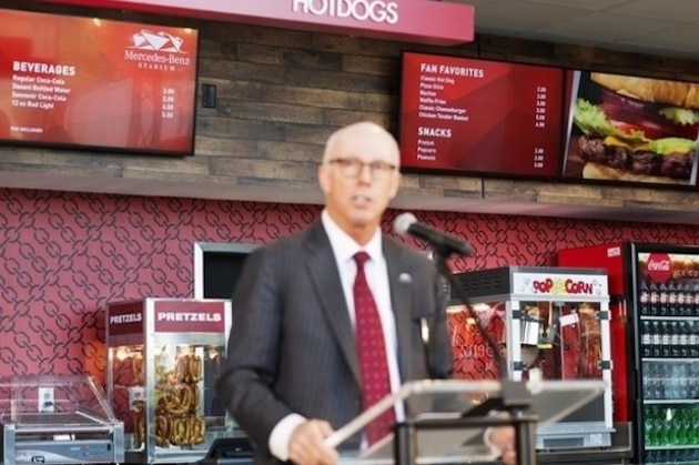 Proposed concession stand menu prices are displayed as Atlanta Falcons president and CEO Rich McKay speaks during a news conference inside the Falcons new stadium currently under construction Monday, May 16, 2016, in Atlanta. Falcons owner Arthur Blank says the Mercedes-Benz Stadium is on schedule to open in June, 2017 as scheduled and he's hoping it will be announced next week as the site of a Super Bowl. The Falcons also unveiled their new food and beverage plan which includes $2 hot dogs and soft drinks, a sharp decrease from current prices at the Georgia Dome. (AP Photo/David Goldman)