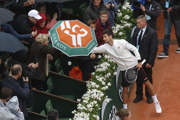Serbia's Novak Djokovic borrows an umbrella from a spectator before resuming his fourth round match of the French Open tennis tournament against Spain’s Roberto Bautista Agut at the Roland Garros stadium in Paris, France, Tuesday, May 31, 2016. (AP Photo/Michel Euler)