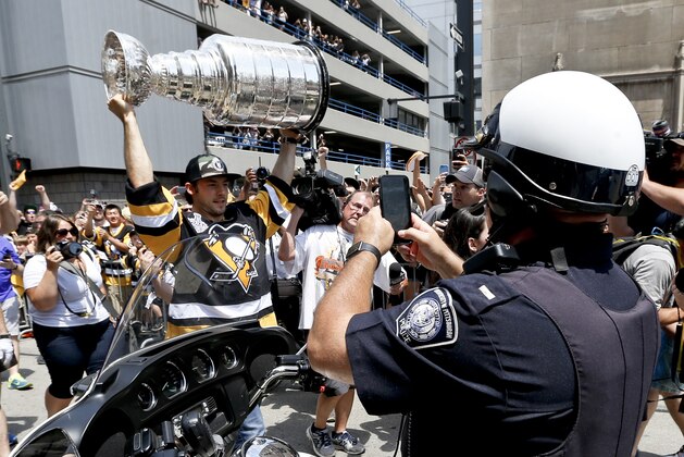 A policeman from the University of Pittsburgh, right, takes a photograph of Pittsburgh Penguins' Kris Letang as he carries the Stanley Cup along the victory parade route in Pittsburgh, Pa., Wednesday, June 15, 2016. The Penguins defeated the San Jose Sharks on Sunday to win the NHL hockey championship. (AP Photo/Keith Srakocic)