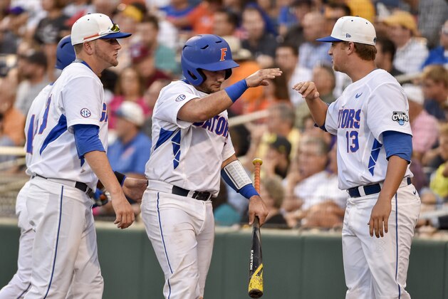 Florida's Mike Rivera, center, is greeted by Kirby Snead (13) and Mike Fahrman, left, after he scored on a single by Ryan Larson during the fourth inning of an NCAA College World Series baseball game against Miami in Omaha, Neb., Saturday, June 13, 2015. (AP Photo/Mike Theiler)