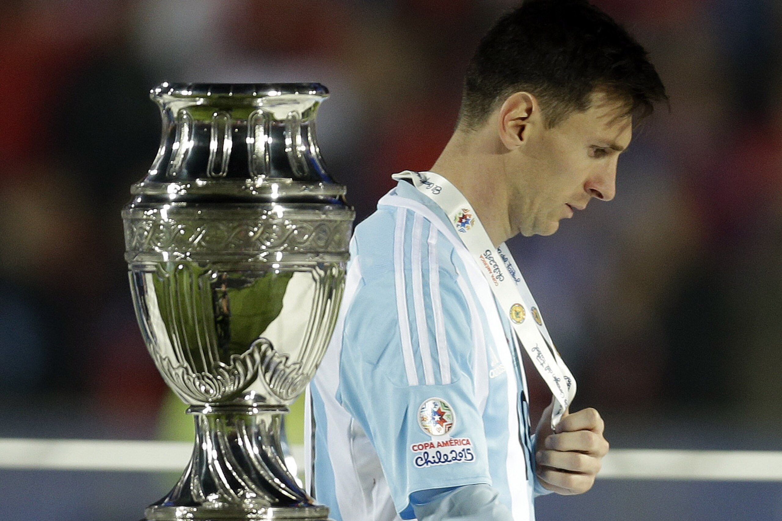FILE - In this July 4, 2015, file photo, Argentina's Lionel Messi walks by the Copa America trophy after receiving the silver medal after the final game with Chile at the National Stadium in Santiago, Chile. Chile goalkeeper Claudio Bravo made a save and striker Alexis Sanchez converted the winning penalty as host Chile defeated Argentina 4-1 in a shootout after a 0-0 draw in the Copa America final.(AP Photo/Natacha Pisarenko, File)