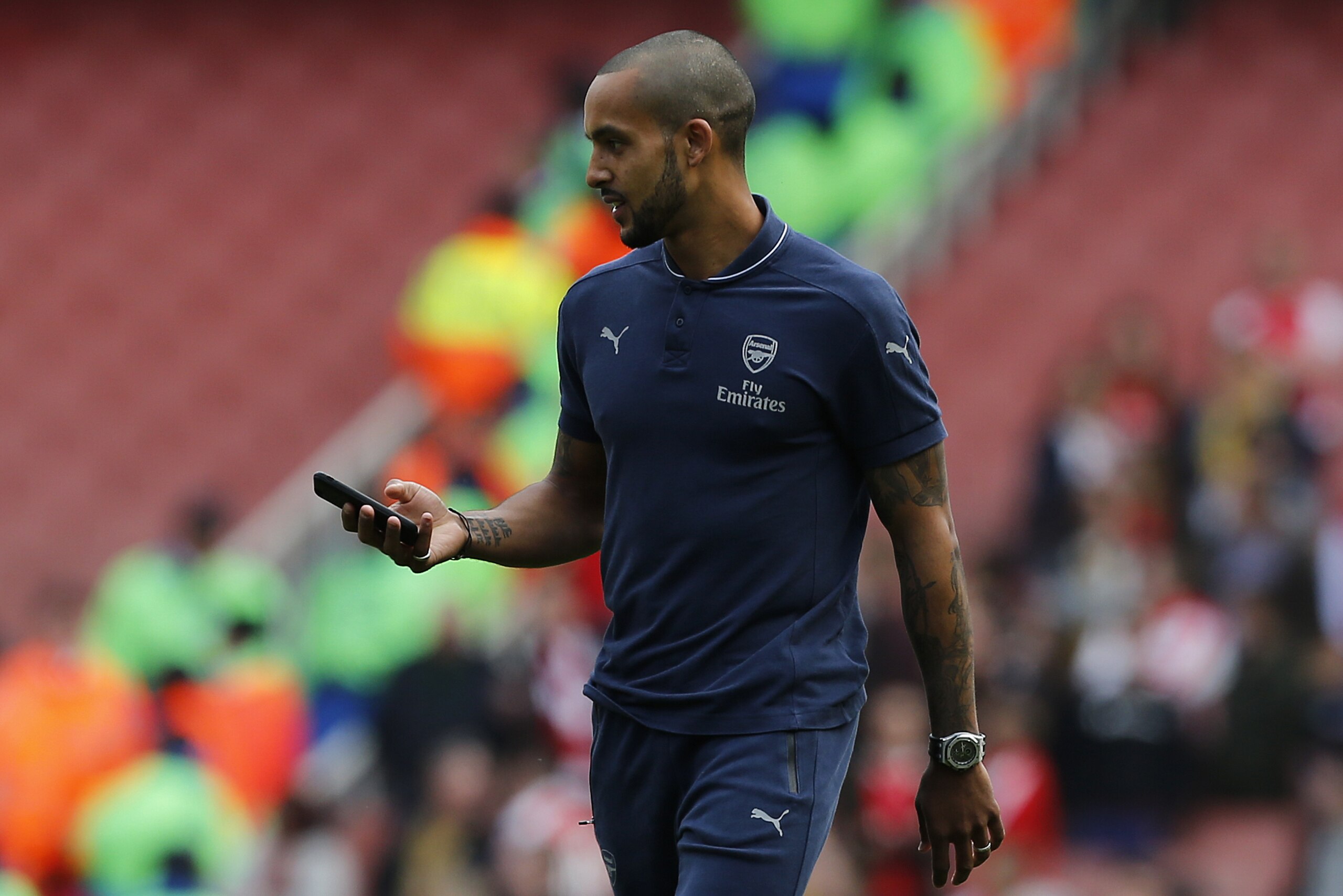 Arsenal's English midfielder Theo Walcott carrys a mobile phone as he walks around the pitch following the English Premier League football match between Arsenal and Aston Villa at the Emirates Stadium in London on May 15, 2016.  / AFP / Ian Kington / RESTRICTED TO EDITORIAL USE. No use with unauthorized audio, video, data, fixture lists, club/league logos or 'live' services. Online in-match use limited to 75 images, no video emulation. No use in betting, games or single club/league/player publications.  /         (Photo credit should read IAN KINGTON/AFP/Getty Images)