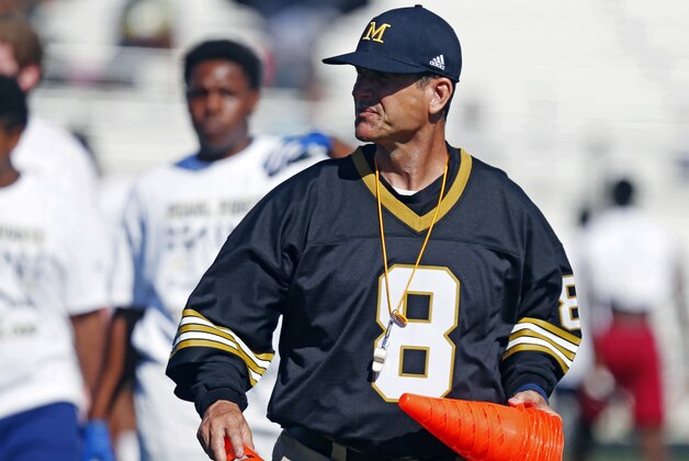Ever the hands-on leader, Michigan football coach Jim Harbaugh places the marker cones on the Pearl High School football field in preparation for a number of agility and speed speed drill, Wednesday, June 8, 2016 at a Michigan Satellite Camp at Pearl High School in Pearl, Miss. Satellite camps continue to be a controversial issue in college football with one side believing they are a great way to generate opportunities for high school prospects and the other side that believes they must be better regulated so coaches do not gain an edge in recruiting. (AP Photo/Rogelio V. Solis)