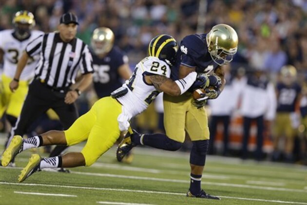 Michigan defensive back Delonte Hollowell, left, tackles Notre Dame wide receiver Amir Carlisle during the first half of an NCAA college football game in South Bend, Ind., Saturday, Sept. 6, 2014. (AP Photo/Michael Conroy)