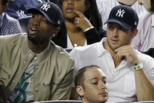 Miami Heat's Dwayne Wade, left, sits beside New York Jets quarterback Tim Tebow during the New York Yankees baseball game against the Los Angeles Angels at Yankee Stadium in New York, Sunday, April 15, 2012. (AP Photo/Kathy Willens)
