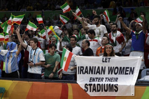 CORRECTS NAME TO DARYA SAFAI INSTEAD OF SARAI DARYA - Fans cheer and wave the flag of Iran as Darya Safai, right, holds a large sign protesting the fact that women have not been allowed to attend volleyball matches in Iran during a men's preliminary volleyball match between Egypt and Iran at the 2016 Summer Olympics in Rio de Janeiro, Brazil, Saturday, Aug. 13, 2016. (AP Photo/Jeff Roberson)