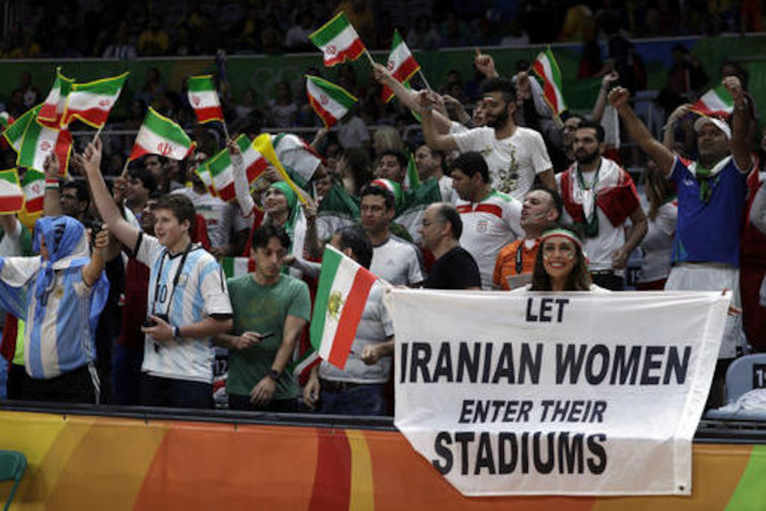 CORRECTS NAME TO DARYA SAFAI INSTEAD OF SARAI DARYA - Fans cheer and wave the flag of Iran as Darya Safai, right, holds a large sign protesting the fact that women have not been allowed to attend volleyball matches in Iran during a men's preliminary volleyball match between Egypt and Iran at the 2016 Summer Olympics in Rio de Janeiro, Brazil, Saturday, Aug. 13, 2016. (AP Photo/Jeff Roberson)