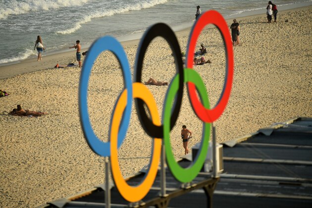 TOPSHOT - People are pictured walking along Copacaba beach through a set of Olympic rings, from during the men's beach volleyball qualifying match between Latvia and Cuba at the Beach Volley Arena in Rio de Janeiro on August 9, 2016, during the Rio 2016 Olympic Games. / AFP / Leon NEAL        (Photo credit should read LEON NEAL/AFP/Getty Images)