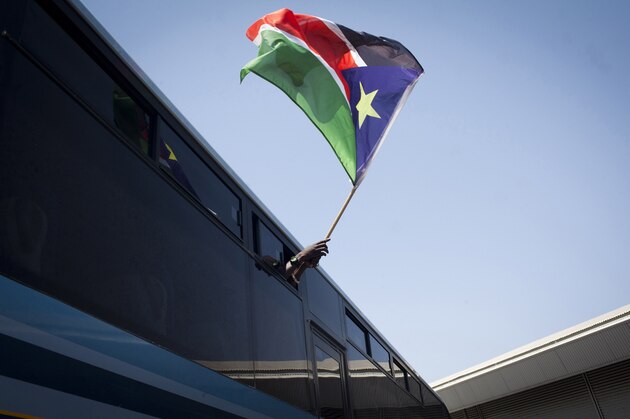 A South Sudanese refugee waves his national flag as they board a bus taking them to Ben Gurion International airport, near Tel Aviv, where they will be deported to South Sudan, on June 17, 2012.  Israel was preparing to fly home about 120  illegal immigrants from South Sudan, the first wave in the planned expulsion of tens of thousands of Africans, officials said. AFP PHOTO/OREN ZIV =ISRAEL OUT=        (Photo credit should read OREN ZIV/AFP/GettyImages)