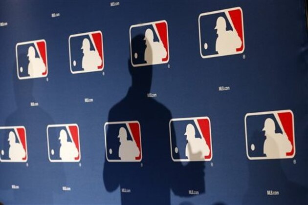 FILE - In this Monday, Feb. 23, 2015 file photo, the shadow of MLB Commissioner Rob Manfred is projected on an MLB logo backdrop in Phoenix. Major league teams steeply increased the money spent on young players in 2015, but the overall percentage of revenue devoted to players has remained relatively stable for a decade. (AP Photo/Ross D. Franklin)