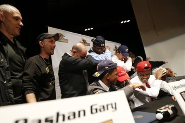 Graduating high school football players from Paramus Catholic High School, right, and coaches, left, pose for photographs with defensive tackle Rashan Gary, top center, a top high school football recruit, during a rally following Gary's television announcement in which he declared he intends on playing college football at Michigan, on national signing day, Wednesday, Feb. 3, 2016, in Paramus, N.J. (AP Photo/Julio Cortez)